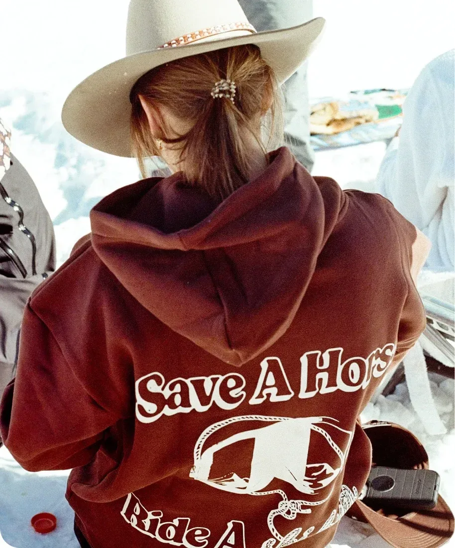 A woman in a cowboy hat wearing a Raw & Rebellious “Save A Horse” hoodie